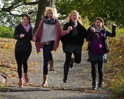 vier Frauen auf einem Waldweg springen hüpfend und lachend auf die Kamera zu