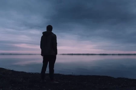 Abenddämmerung. Mann ist von hinten zu sehen. Blickt über den See in die Ferne